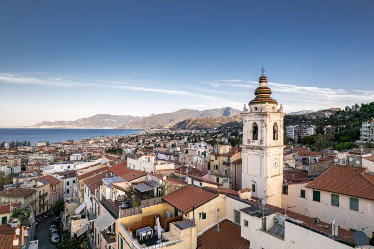 Il campanile bianco di Bordighera Alta sopra i tetti rossi, con la città, il mare e la costa verso la Francia