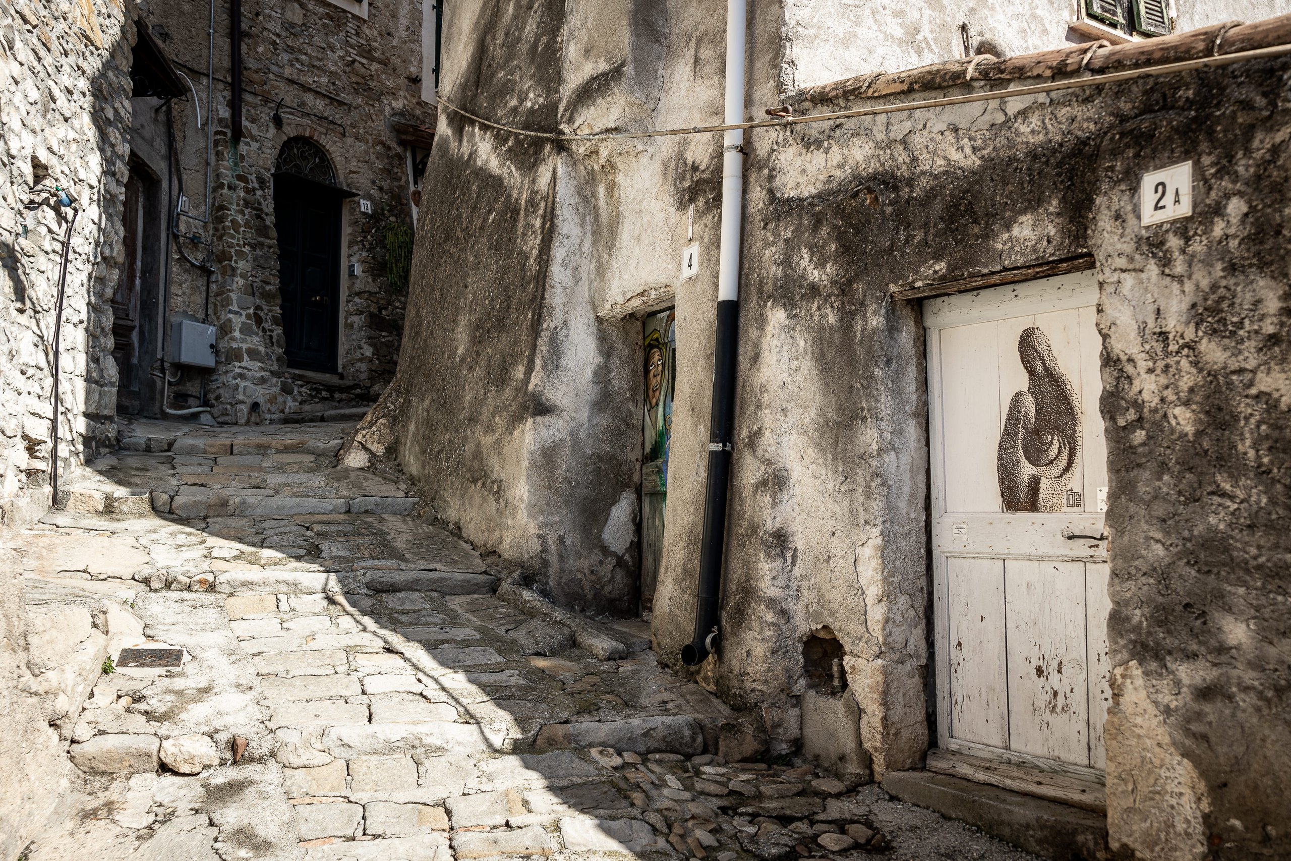 A stone carruggio in Borghetto San Nicolò with two painted doors, between old walls and uneven paving