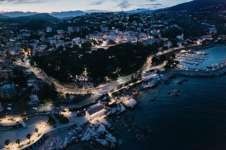 Vista aerea di Capo Sant'Ampelio, dell'anfiteatro e del porto illuminati al crepuscolo, con Bordighera e le montagne