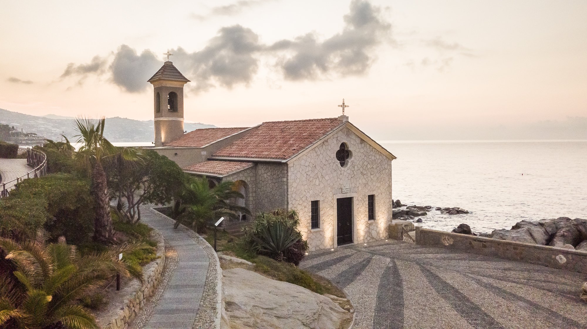 Chiesetta di Sant'Ampelio con campanile, tetto in coppi e sagrato in ciottoli, vista dall'alto con il mare alle spalle