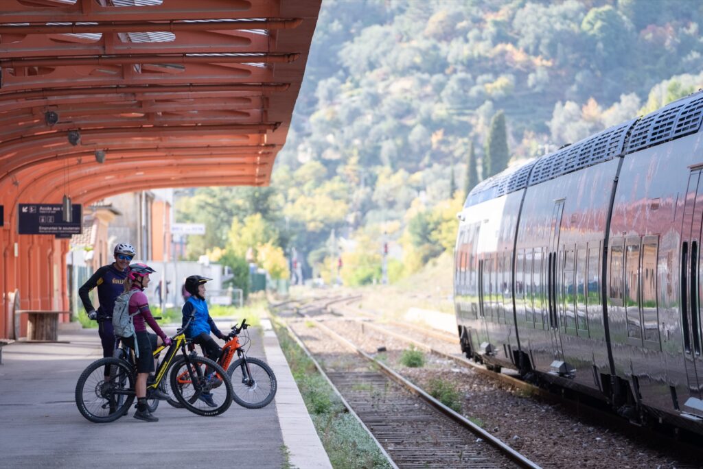 Three cyclists with e-bikes on the platform of a Valle Roya station next to the train