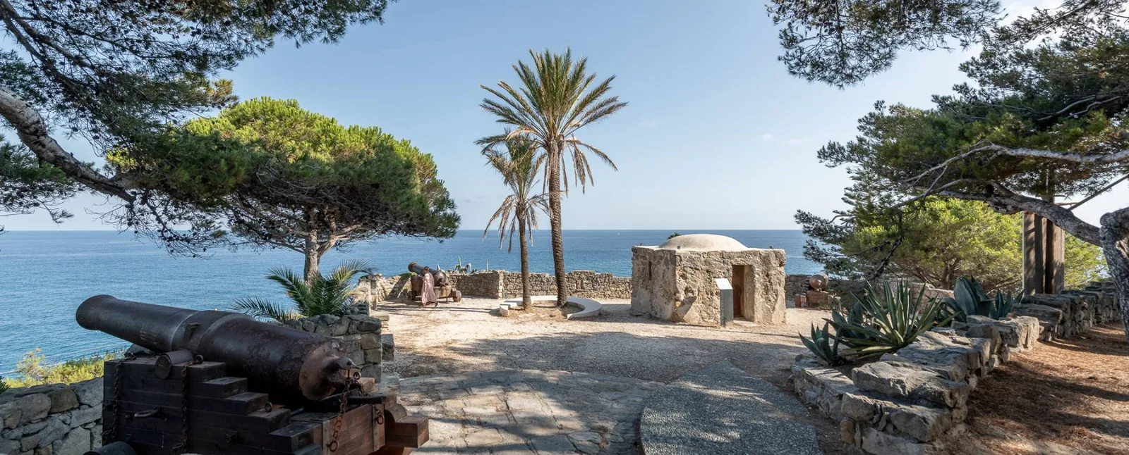 Antichi cannoni tra pini e palme sul promontorio affacciato sul mare