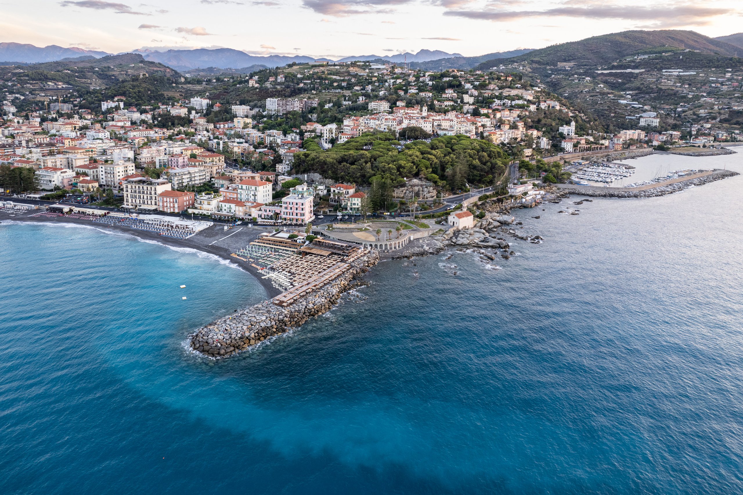 Vista aerea di Capo Sant'Ampelio con il pennello di scogli, la spiaggia, la pineta del Capo e il porto di Bordighera all'alba