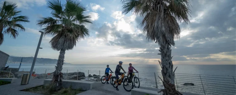 Ciclisti in e-bike sul lungomare di Bordighera tra le palme