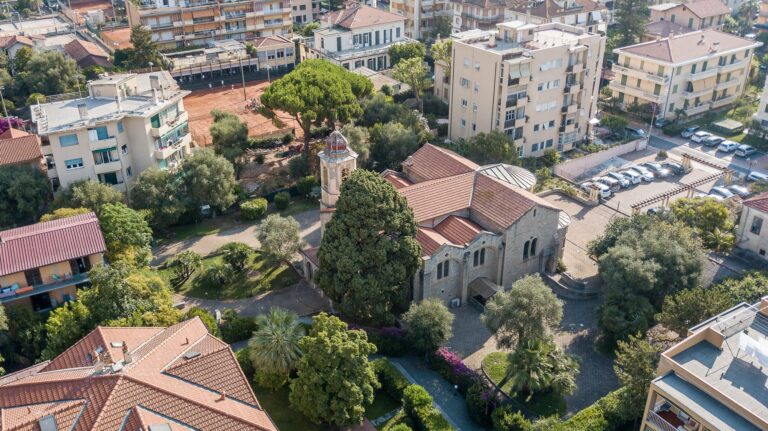 Vista aerea dell'ex Chiesa Anglicana tra cipressi, pini e palazzi, con i campi da tennis in terra rossa accanto