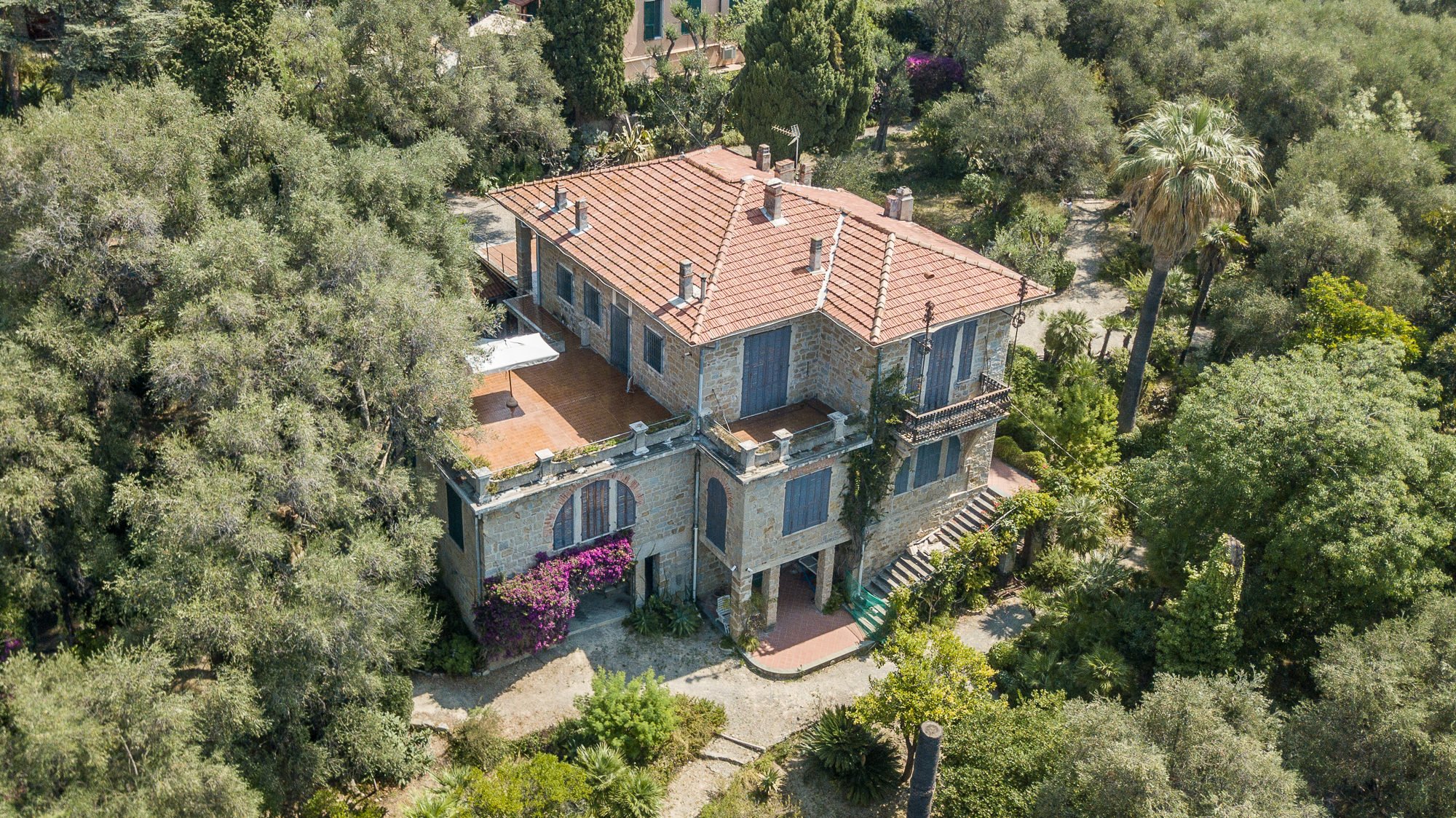 Vista aerea della villa in pietra della Fondazione Pompeo Mariani con terrazze, buganvillea e il fitto giardino di olivi