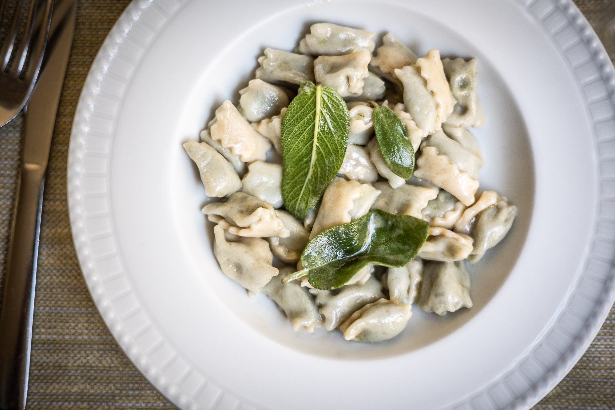 White soup plate of homemade ravioli dressed with sage leaves