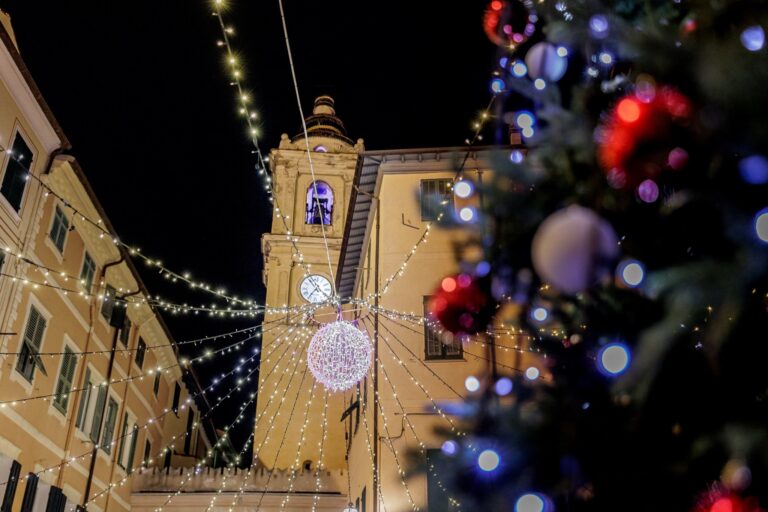 Il campanile di Bordighera Alta con la sfera luminosa, visto oltre le palline sfocate dell'albero di Natale