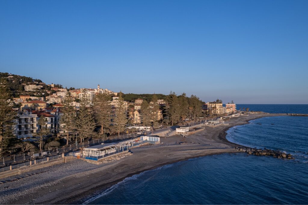 Vista aerea del lungomare con il filare di araucarie, la spiaggia, gli stabilimenti e Bordighera sulla collina
