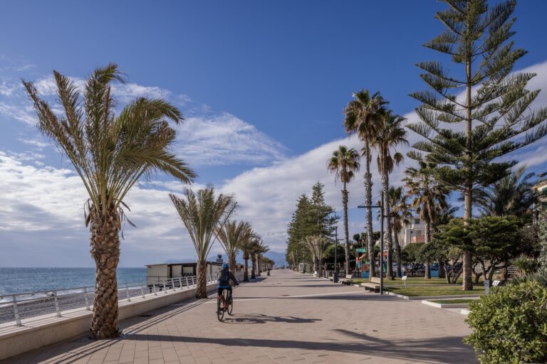 Il nuovo lungomare di Bordighera con la passeggiata pavimentata, palme, araucarie, un ciclista e il mare