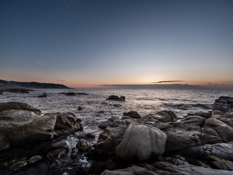 Scogli di arenaria levigati dal mare all'alba sulla costa di Bordighera, con il cielo sfumato