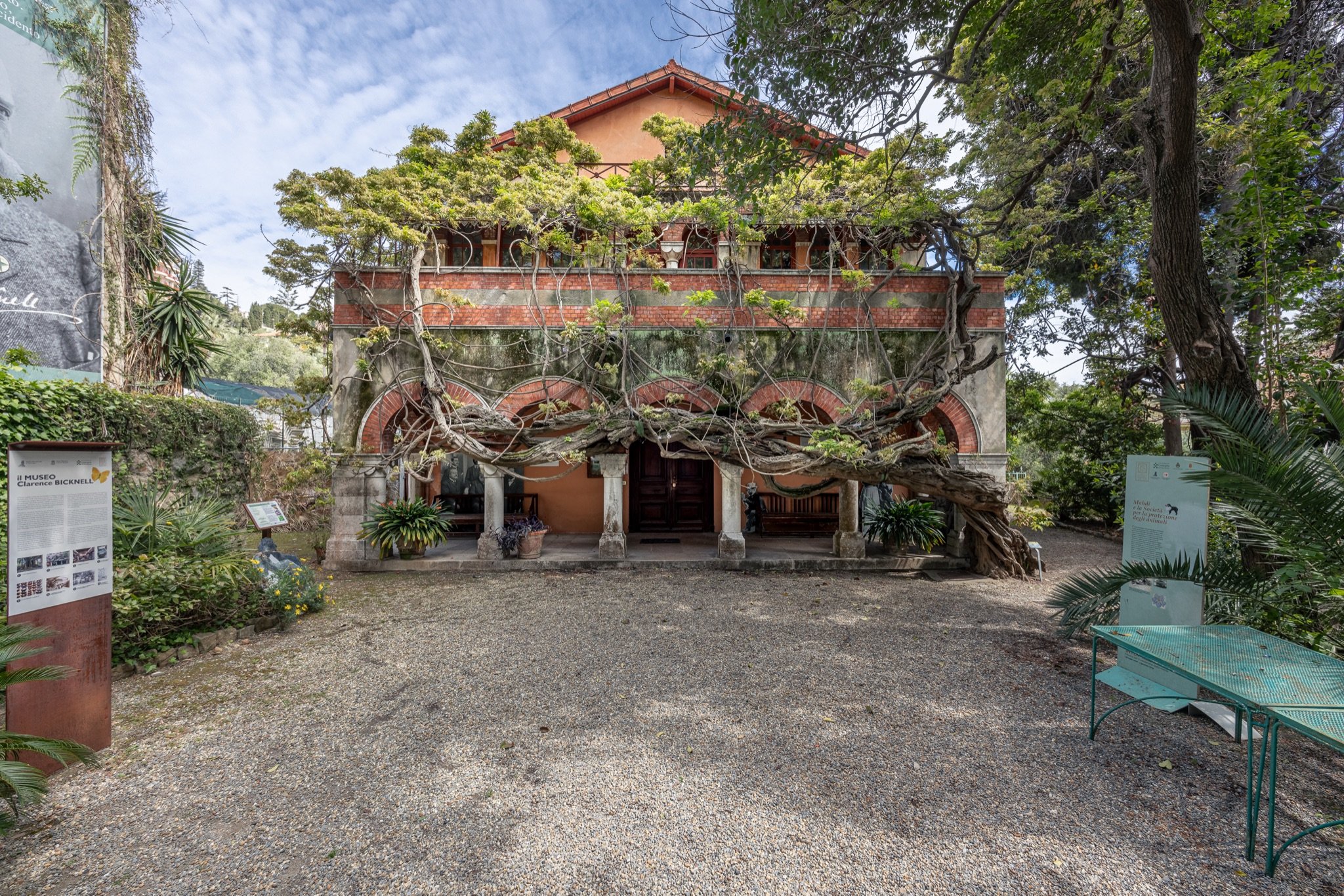Facciata del Museo Bicknell con il portico ad archi coperto dal glicine, il piazzale in ghiaia e un tavolo verde