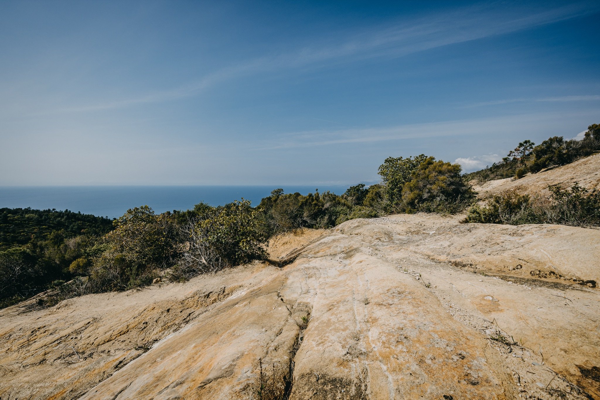 Placche di arenaria dorata con una fenditura, macchia mediterranea e il mare all'orizzonte sul Monte Nero