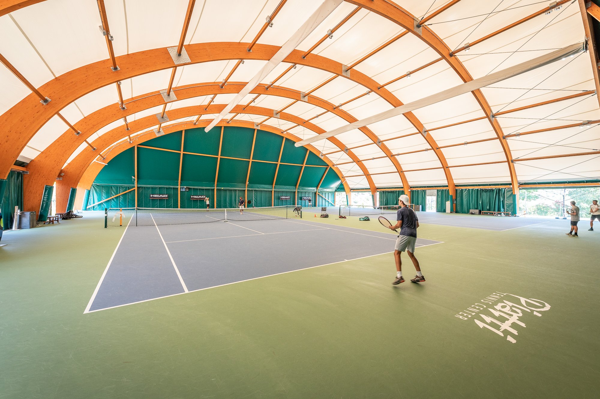 Campo da tennis coperto del Piatti Tennis Center con travi ad arco in legno lamellare e un giocatore