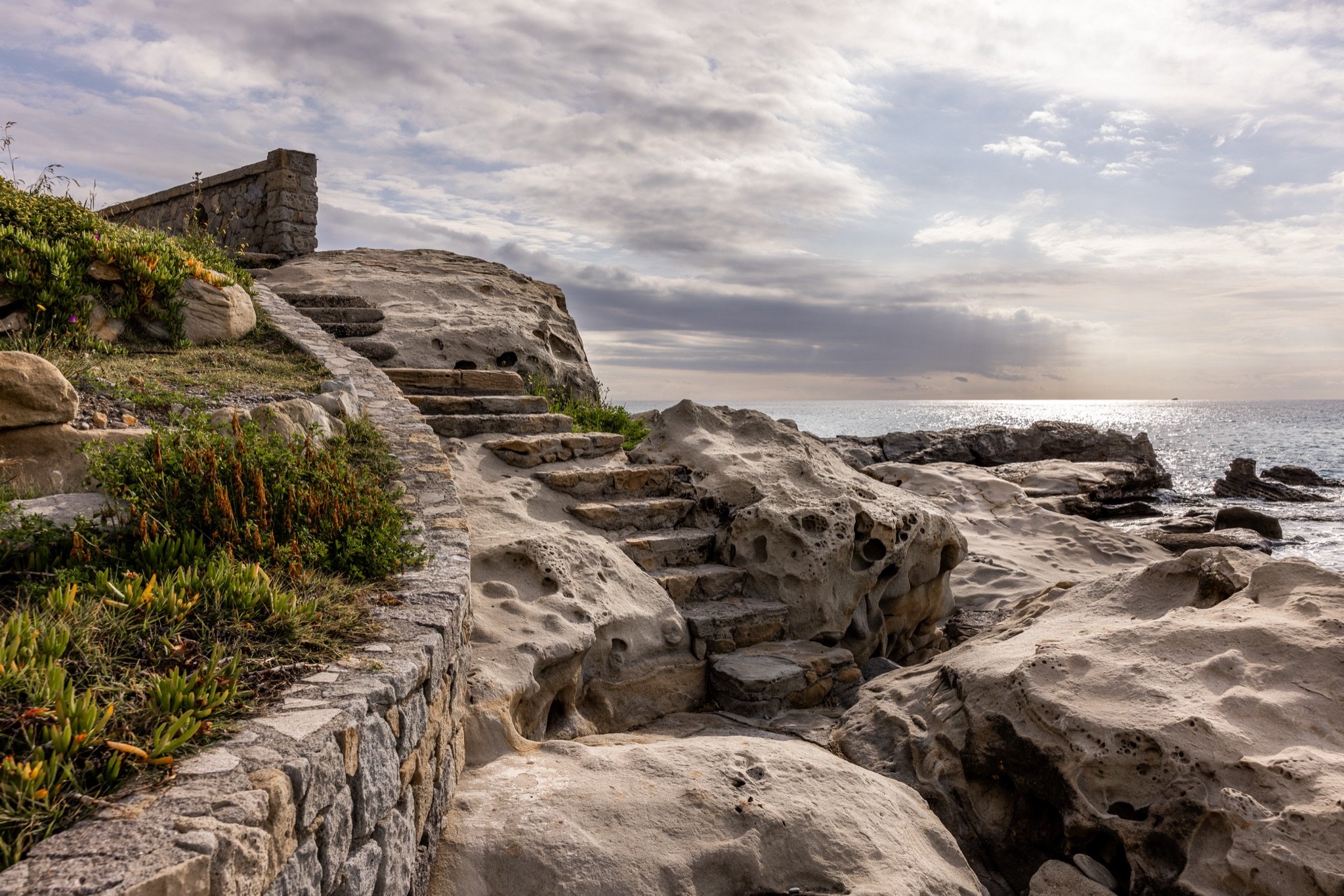 Scalinata scavata nelle rocce di arenaria alveolata di Capo Sant'Ampelio, con il mare e il cielo nuvoloso