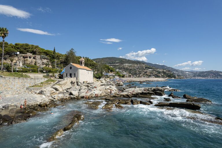 Le onde sugli scogli davanti alla chiesetta di Sant'Ampelio, con la costa verso levante e le colline