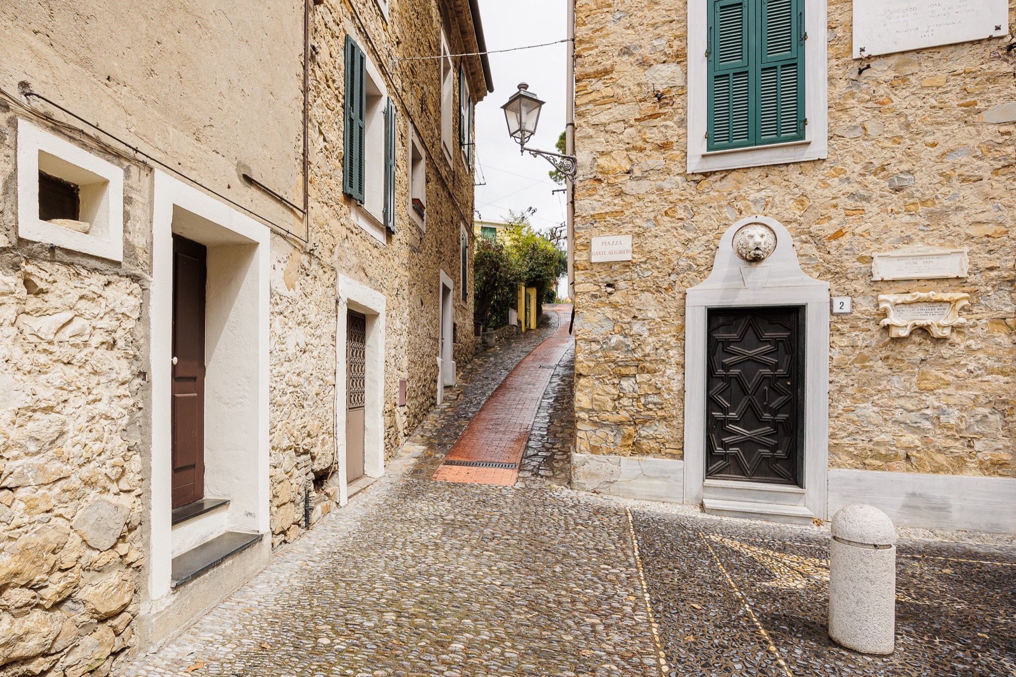 Exposed-stone houses in the village of Sasso with a carved doorway and an uphill brick-paved carruggio