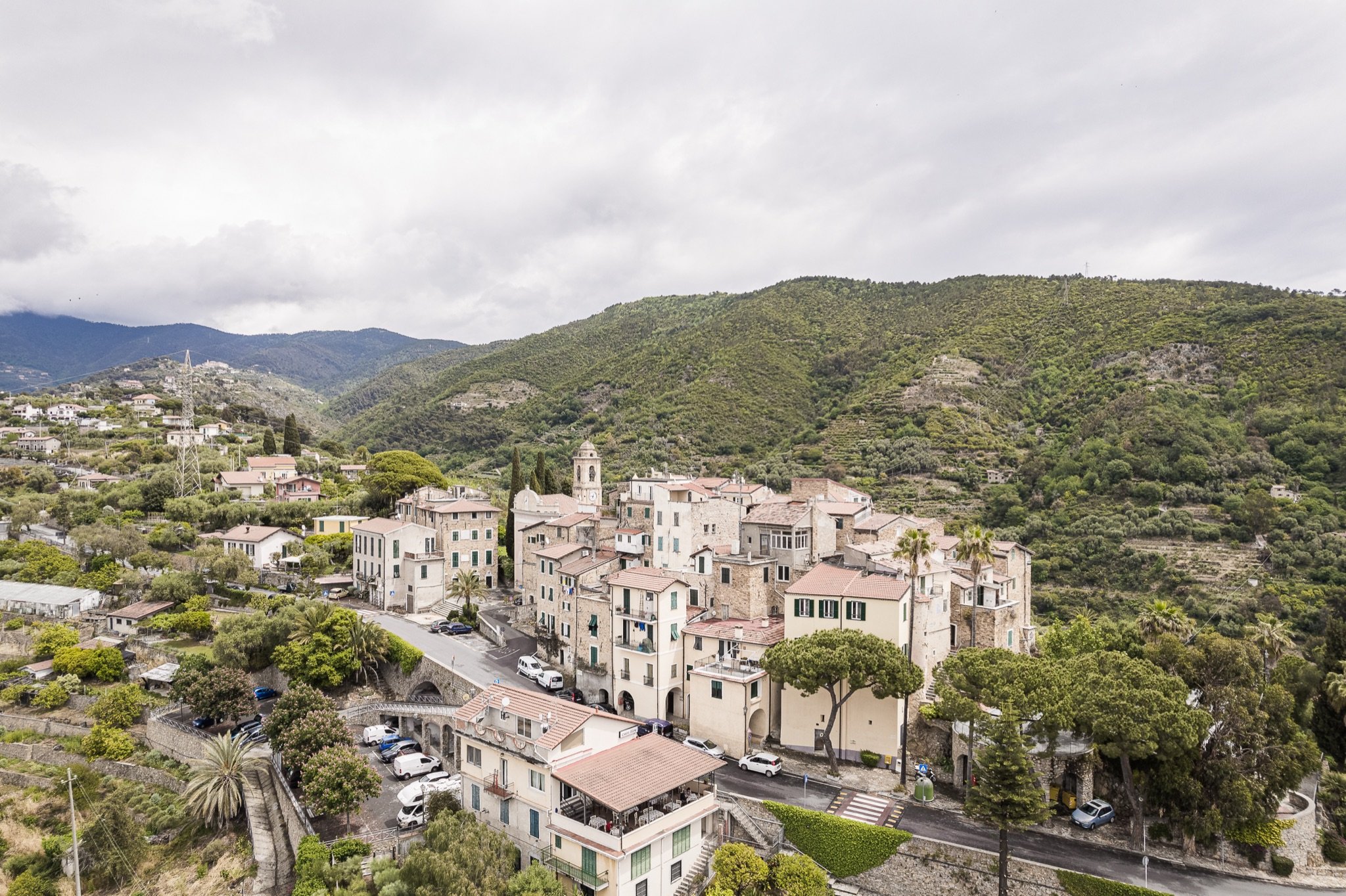 Aerial view of the village of Sasso among green hills, olive trees and scattered houses, with mountains in the background