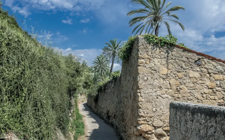 Ein Fußweg zwischen Steinmauern, Palmen und Grün in Bordighera
