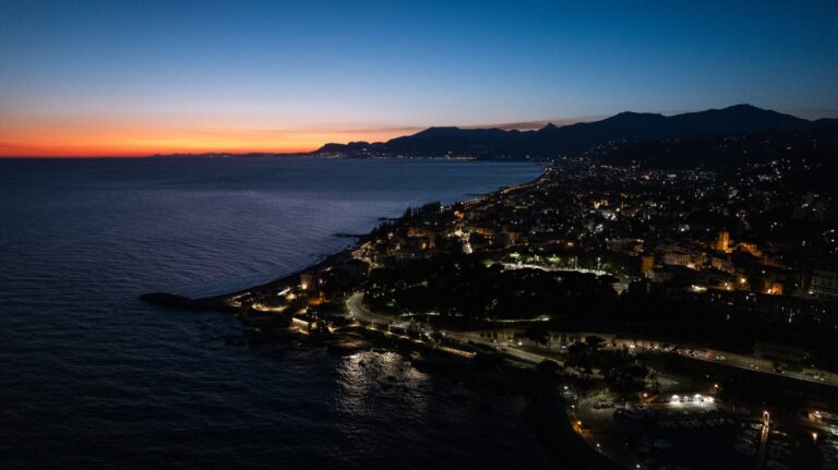 Vista aerea di Capo Sant'Ampelio e della città illuminata al crepuscolo, con il mare e la costa verso Sanremo