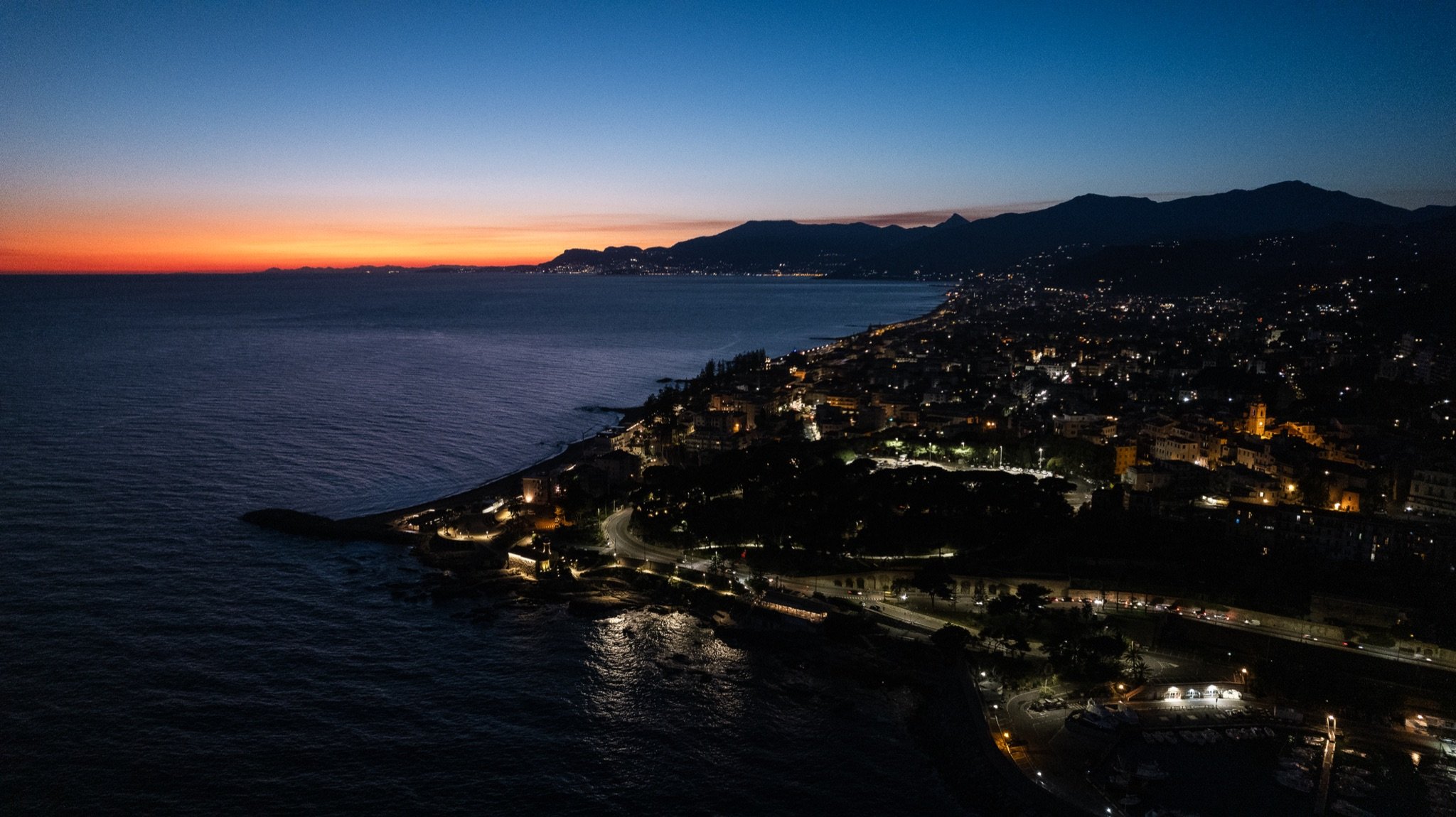 Luftaufnahme des Capo Sant’Ampelio und des beleuchteten Bordighera in der Abenddämmerung, mit dem Meer und der Küste Richtung Sanremo