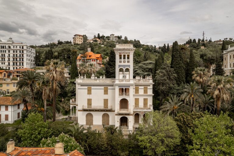 Villa Etelinda vista frontalmente dal drone, con la torre, le logge ad archi e il parco di palme e cipressi