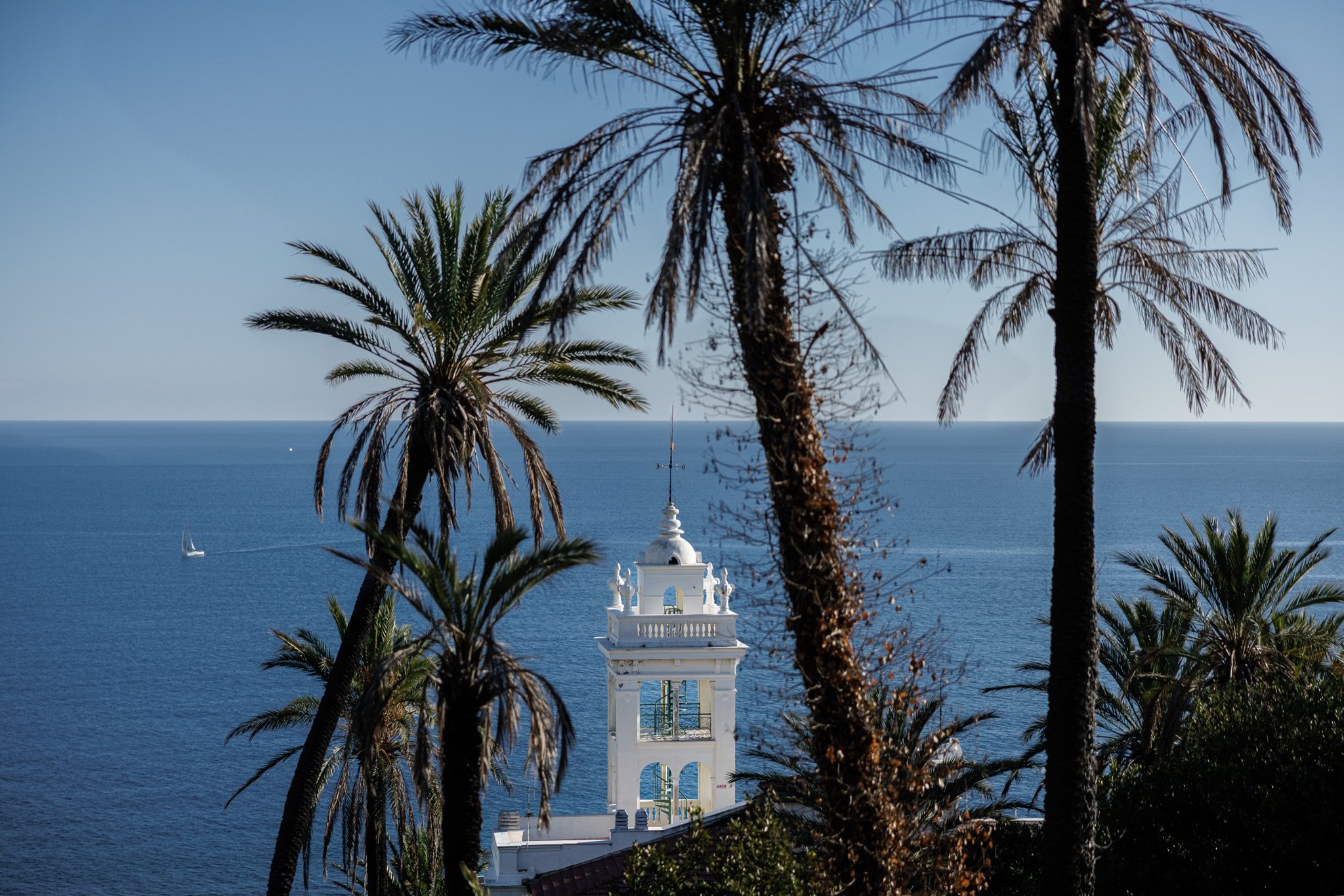 La torre di Villa Garnier tra le palme con il mare blu e una barca a vela all'orizzonte