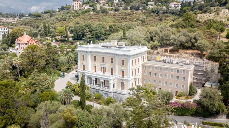 Vista aerea di Villa Regina Margherita con la facciata color crema, l'edificio annesso e il parco con cipressi e palme