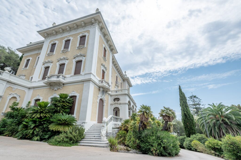 Villa Regina Margherita con facciata color crema, cornici bianche, scalinata d'ingresso, palme e cipressi nel giardino