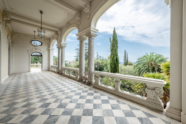 Loggia di Villa Regina Margherita con archi, colonne in marmo, lampade e pavimento a scacchi aperta sul giardino con palme