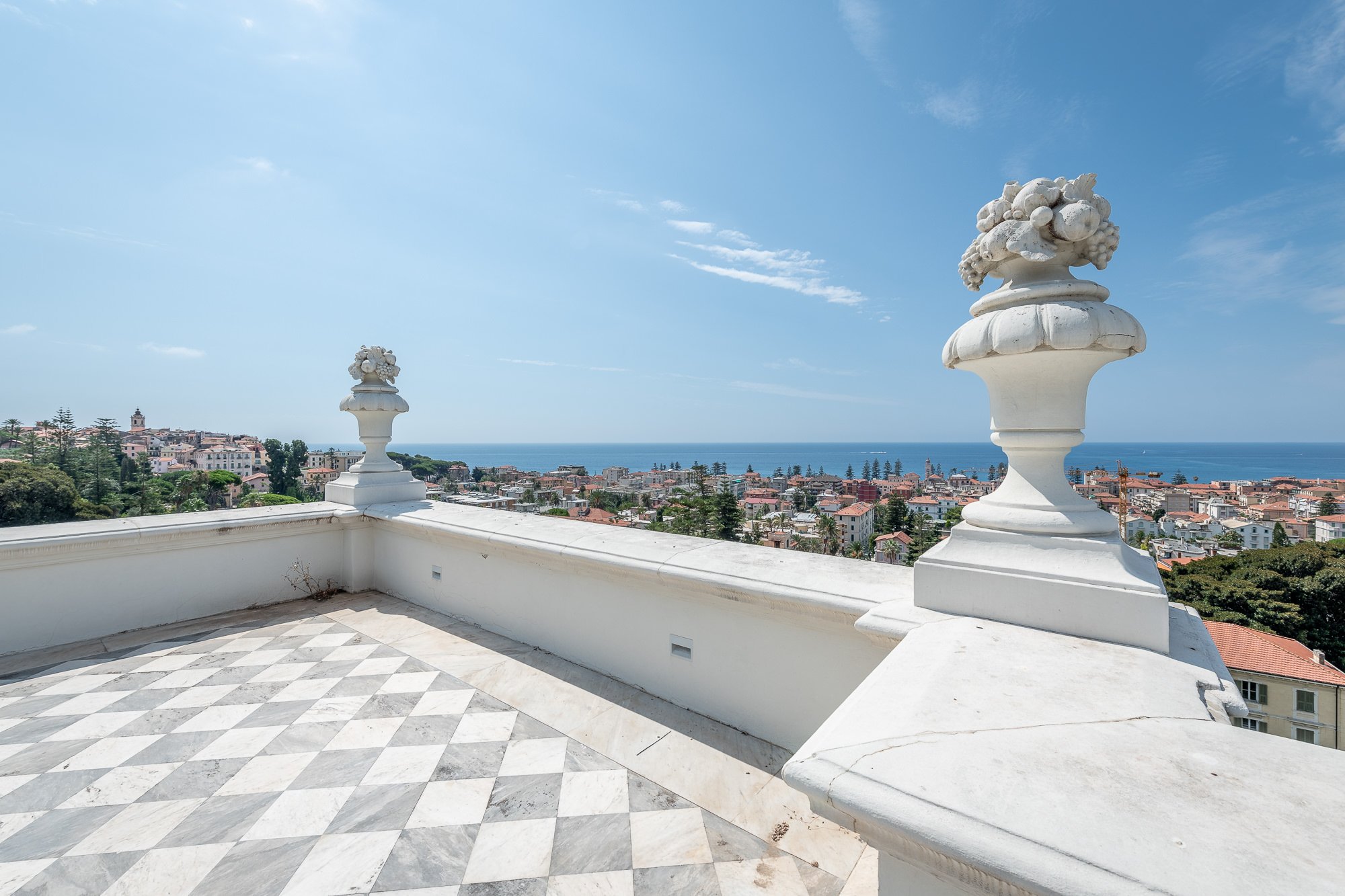 Terrazza sul tetto di Villa Regina Margherita con pavimento a scacchi, balaustra e vasi in marmo, con vista su Bordighera e il mare