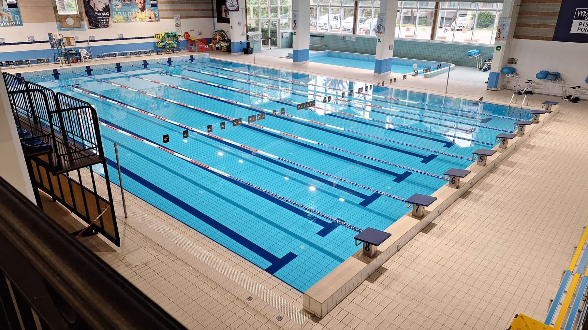 Piscina coperta del Palasport di Bordighera vista dalla tribuna: otto corsie, blocchi di partenza numerati e la vasca piccola in fondo