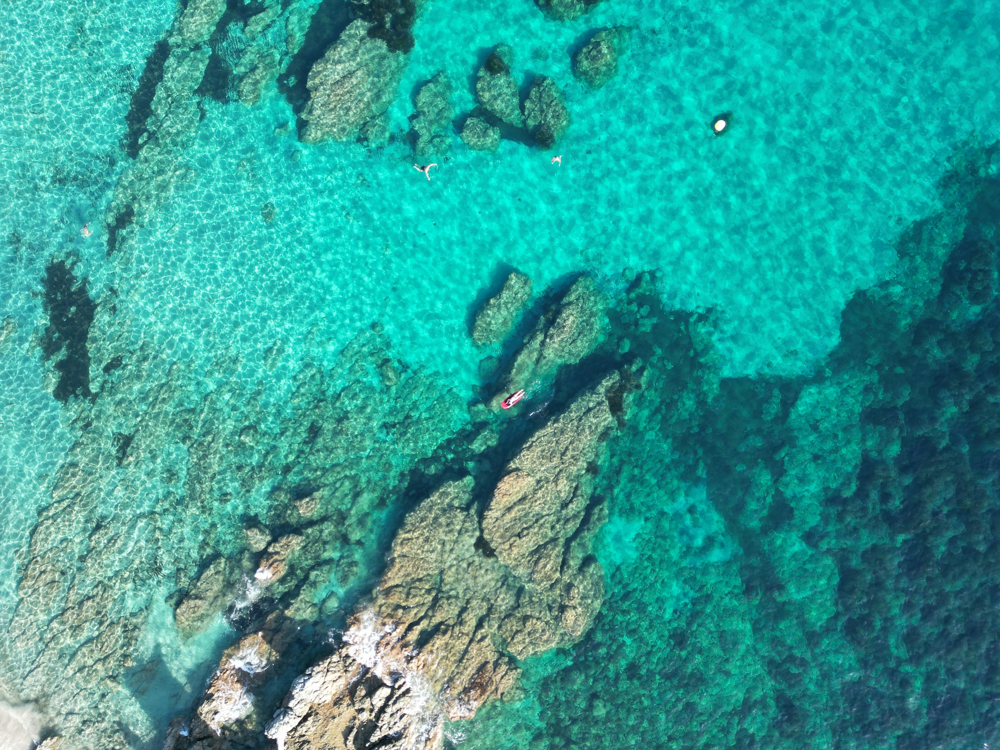Costa rocciosa e acqua turchese con nuotatori, vista dall'alto
